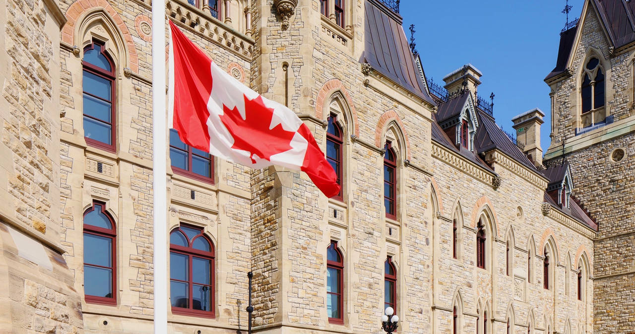 Drapeau canadien à mi-mât devant le bâtiment du Parlement canadien.