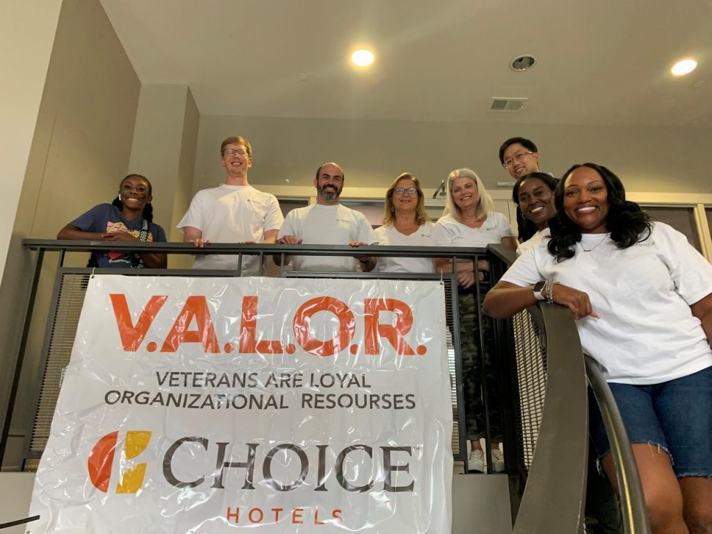 A group of people in white shirts standing on a staircase behind a banner reads V.A.L.O.R.