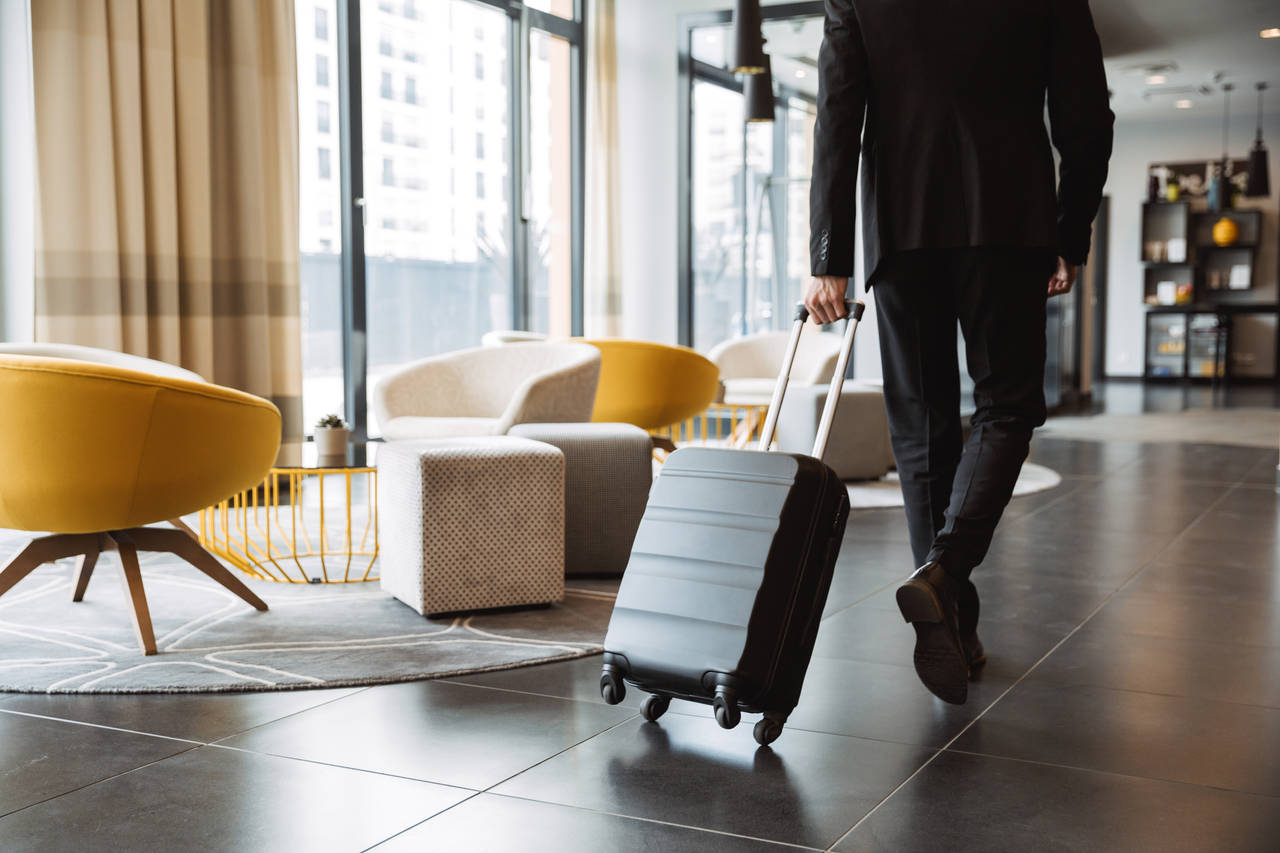 Cropped photo of caucasian businessman wearing formal black suit walking with suitcase in hotel lobby