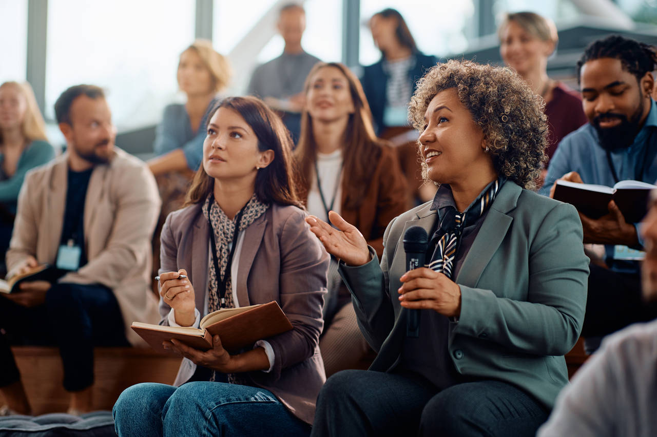 Happy businesswoman talking on microphone while attending education event in conference hall.