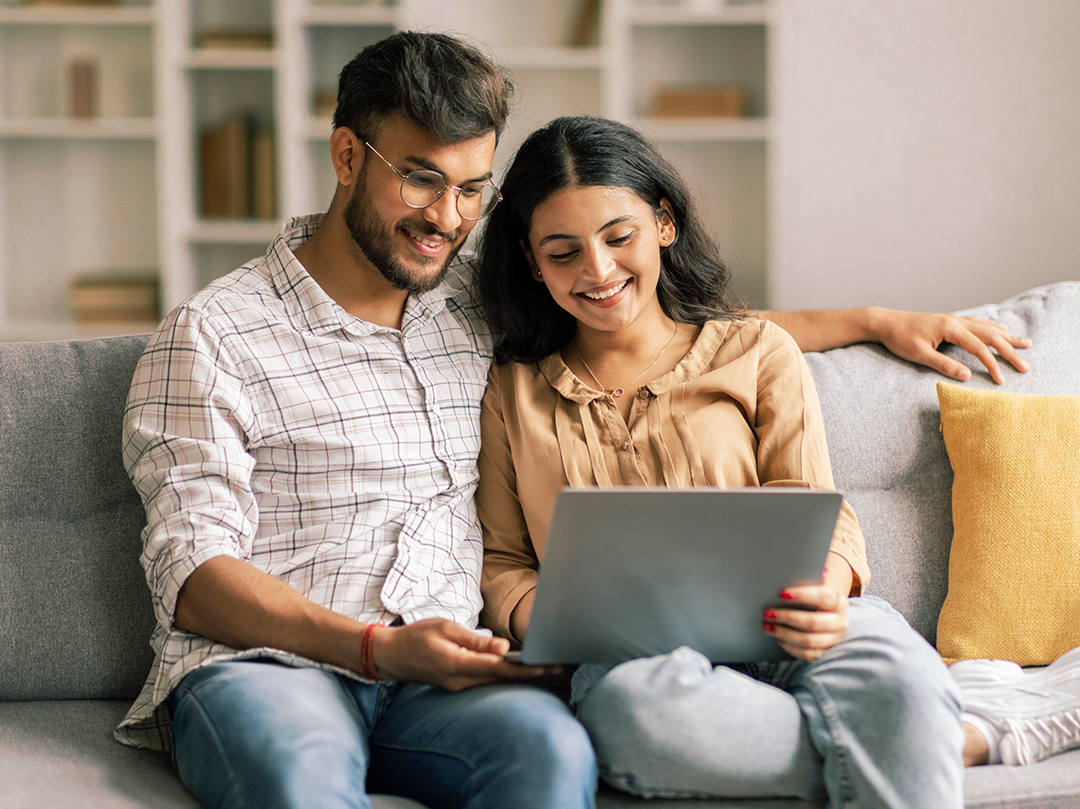 Couple sitting on couch looking ta laptop