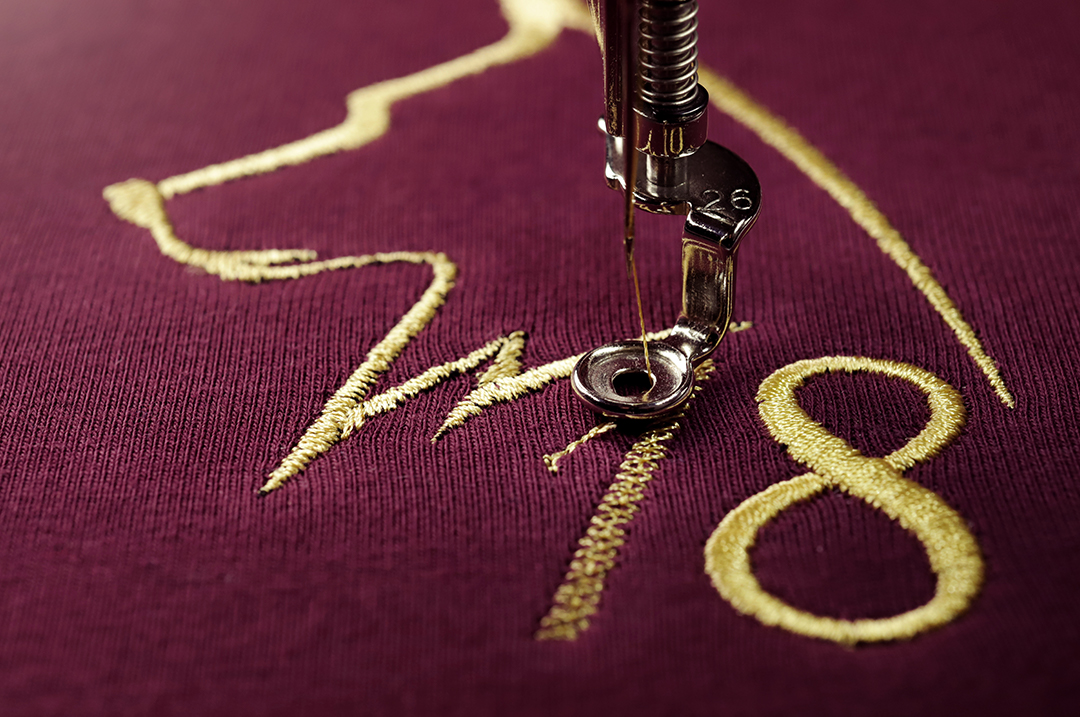 Custom maroon shirt being embroidered in gold with logo designed while planning a group golf trip